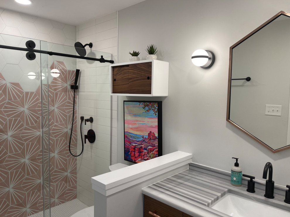 This is an example of a small midcentury kids bathroom in Baltimore with flat-panel cabinets, medium wood cabinets, an alcove shower, a two-piece toilet, pink tile, cement tile, grey walls, porcelain floors, an undermount sink, marble benchtops, white floor, a sliding shower screen, grey benchtops, a niche, a single vanity and a built-in vanity.