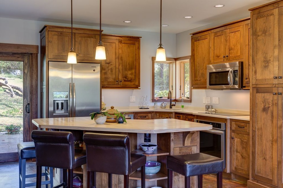 Photo of a mid-sized arts and crafts l-shaped open plan kitchen in Other with an undermount sink, shaker cabinets, dark wood cabinets, solid surface benchtops, stainless steel appliances, concrete floors, with island and brown floor.