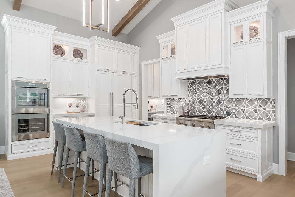 Large transitional u-shaped light wood floor, beige floor, vaulted ceiling and exposed beam eat-in kitchen photo in Columbus with an undermount sink, shaker cabinets, white cabinets, quartz countertops, gray backsplash, marble backsplash, stainless steel appliances, an island and white countertops