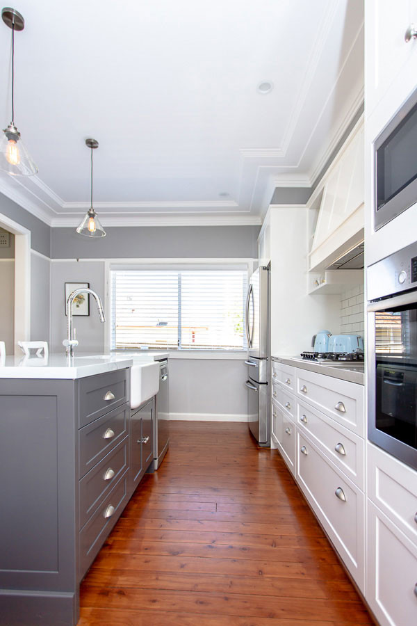Inspiration for a large transitional galley open plan kitchen in Sydney with a farmhouse sink, shaker cabinets, quartz benchtops, white splashback, subway tile splashback, stainless steel appliances, medium hardwood floors, with island, brown floor and multi-coloured benchtop.