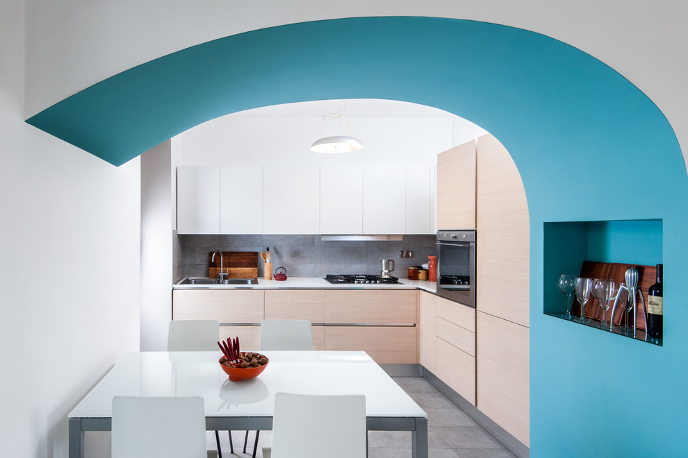 Photo of a contemporary l-shaped eat-in kitchen in Rome with a double-bowl sink, flat-panel cabinets, light wood cabinets, grey splashback, stainless steel appliances, grey floor and white benchtop.