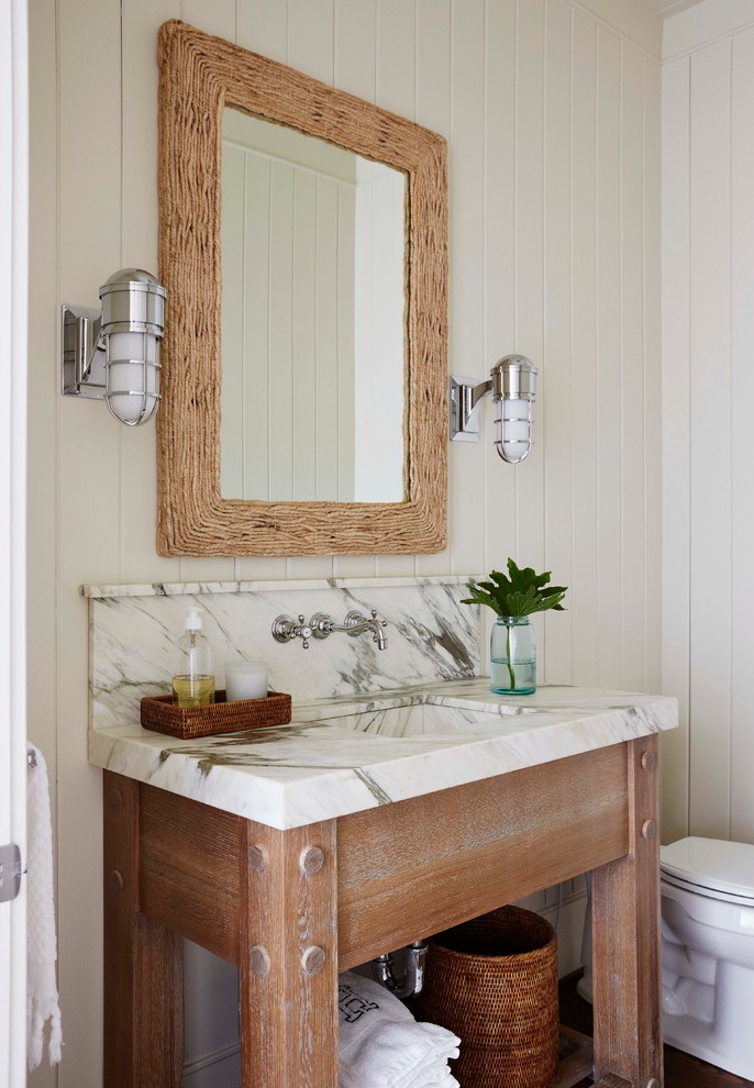 Photo of a beach style powder room in Jacksonville with an integrated sink, open cabinets, medium wood cabinets, beige walls and white benchtops.