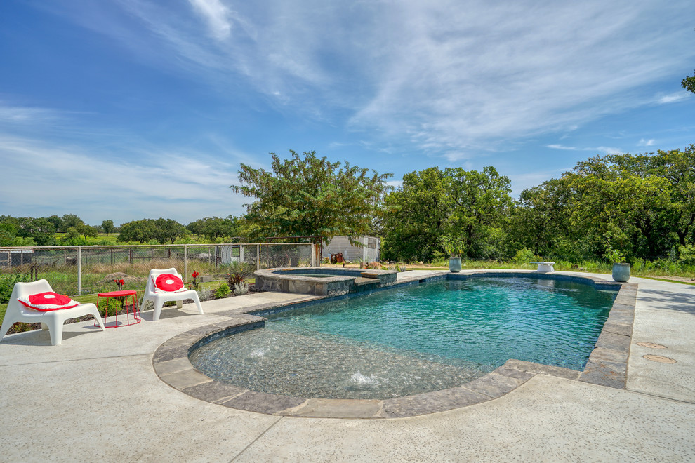Photo of a mid-sized traditional backyard custom-shaped pool in Dallas with a hot tub and concrete slab.