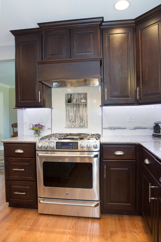 Inspiration for a mid-sized transitional u-shaped light wood floor enclosed kitchen remodel in Chicago with an undermount sink, raised-panel cabinets, dark wood cabinets, quartz countertops, beige backsplash, ceramic backsplash, stainless steel appliances and an island