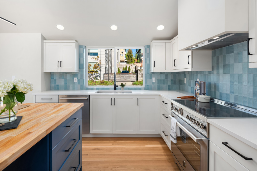 Inspiration for a mid-sized midcentury l-shaped open plan kitchen in Seattle with an undermount sink, shaker cabinets, blue cabinets, wood benchtops, blue splashback, ceramic splashback, stainless steel appliances, medium hardwood floors, with island, brown floor, white benchtop and vaulted.