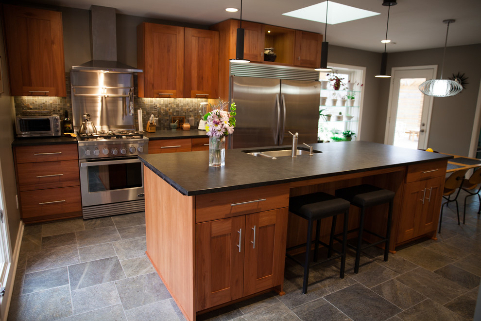This is an example of a mid-sized midcentury single-wall open plan kitchen in Indianapolis with a double-bowl sink, shaker cabinets, dark wood cabinets, soapstone benchtops, grey splashback, stone tile splashback, stainless steel appliances, slate floors, with island and grey floor.