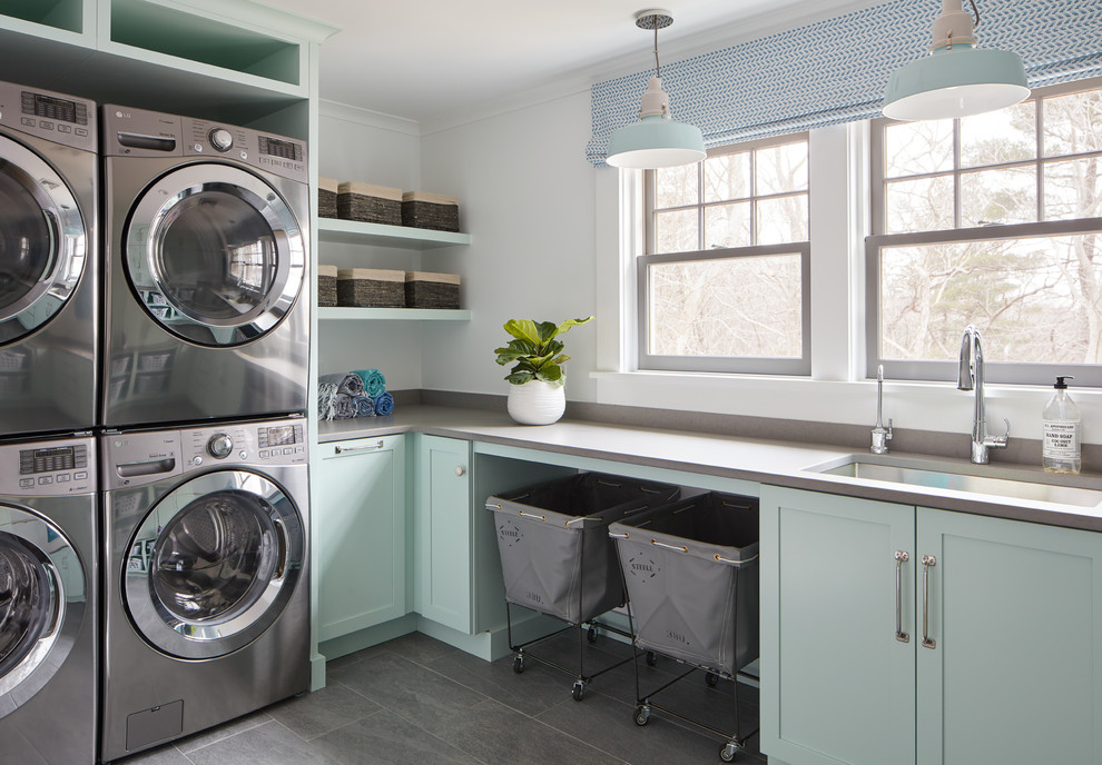 Inspiration for a beach style l-shaped dedicated laundry room in Manchester with an undermount sink, shaker cabinets, green cabinets, white walls, grey floor and grey benchtop.