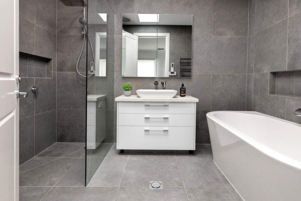 Photo of a large contemporary kids bathroom in Melbourne with flat-panel cabinets, white cabinets, a freestanding tub, gray tile, porcelain tile, porcelain floors, a vessel sink, grey floor, an open shower, white benchtops, a niche, a single vanity, a built-in vanity, an open shower, grey walls and engineered quartz benchtops.