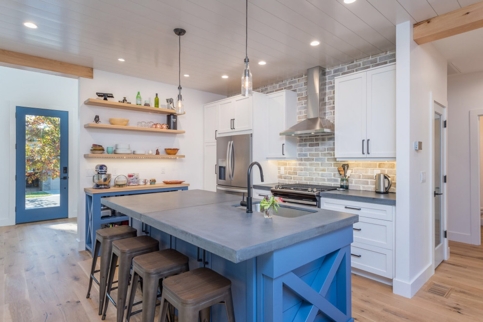 Inspiration for a mid-sized transitional l-shaped eat-in kitchen with an undermount sink, recessed-panel cabinets, white cabinets, concrete benchtops, grey splashback, brick splashback, stainless steel appliances, light hardwood floors, with island, brown floor and grey benchtop.