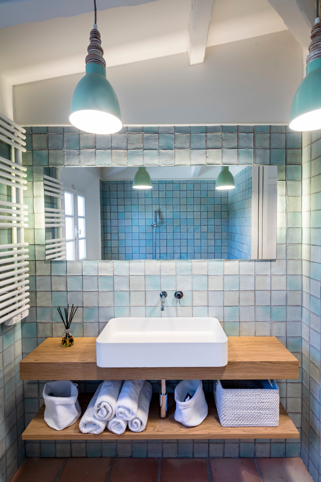 Beach style bathroom with open cabinets, medium wood cabinets, blue tile, blue walls, terra-cotta floors, a vessel sink, wood benchtops and red floor.