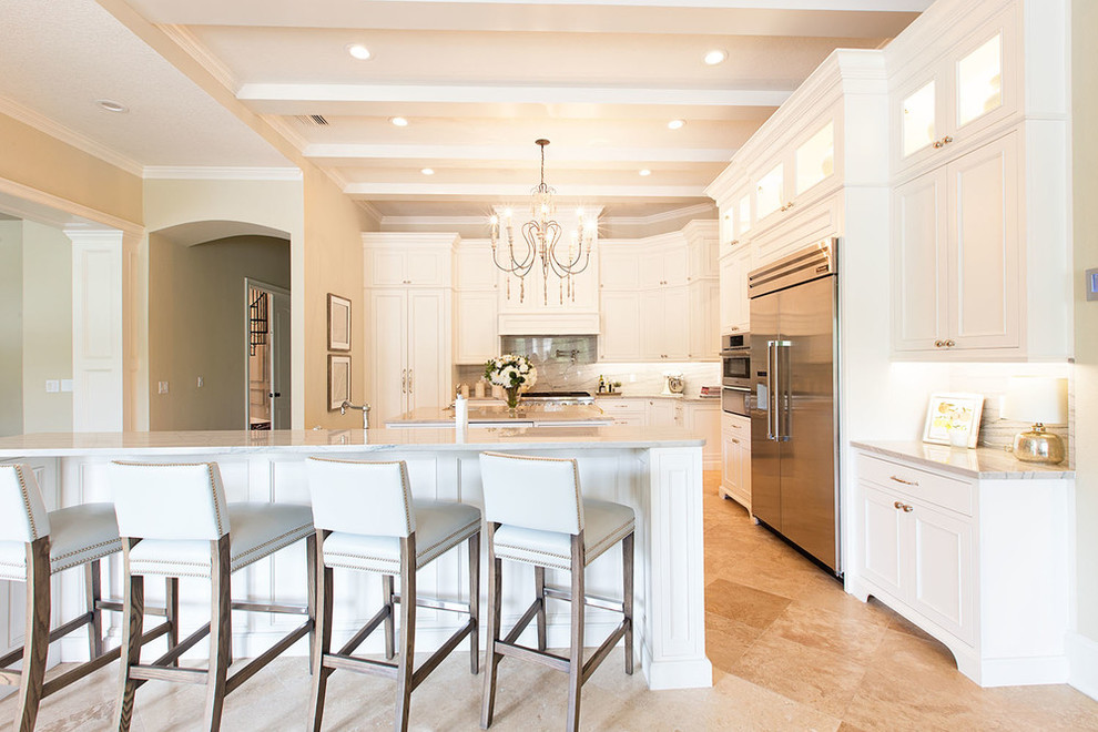 Large transitional l-shaped travertine floor open concept kitchen photo in Orange County with shaker cabinets, white cabinets, marble countertops, white backsplash, stone slab backsplash, stainless steel appliances, two islands and a single-bowl sink