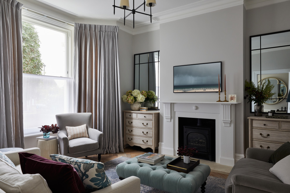 Foto de salón cerrado clásico con paredes grises, suelo de madera en tonos medios, estufa de leña, marco de chimenea de madera y televisor colgado en la pared