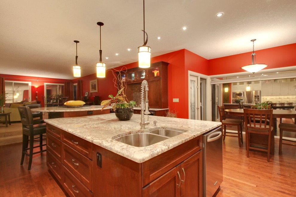 Open concept kitchen - large transitional l-shaped medium tone wood floor and brown floor open concept kitchen idea in Calgary with an undermount sink, recessed-panel cabinets, white cabinets, glass countertops, beige backsplash, matchstick tile backsplash, stainless steel appliances and an island