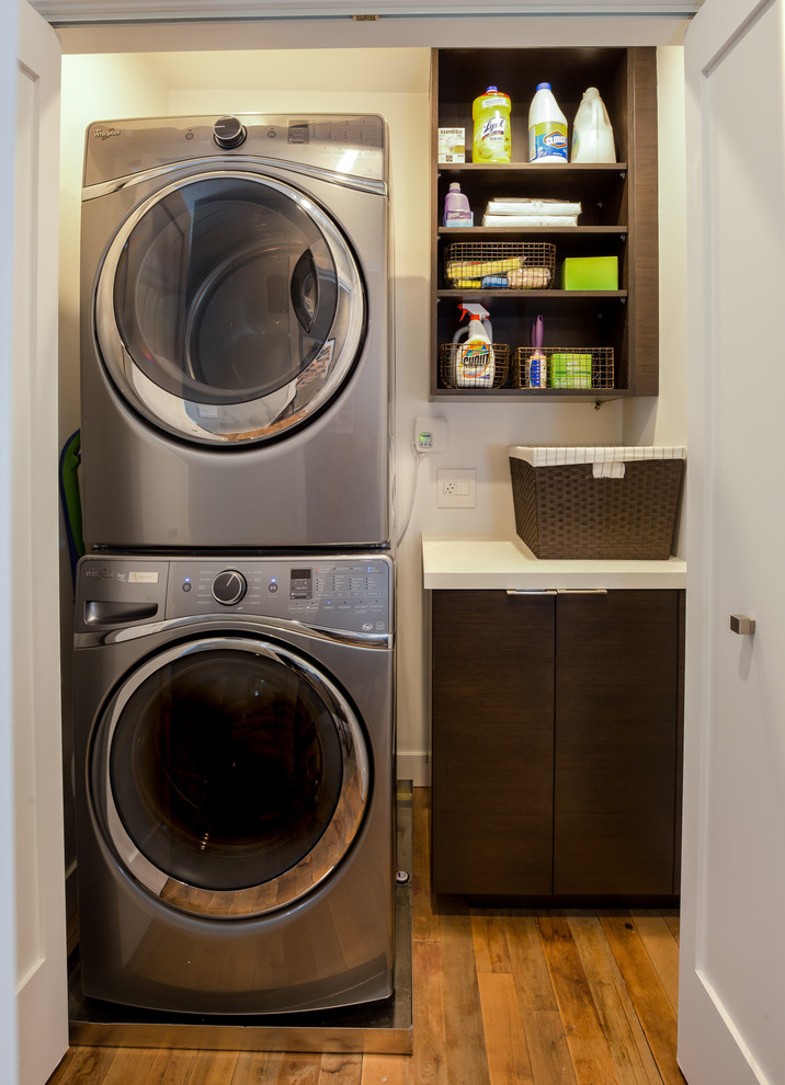 Inspiration for a small transitional single-wall laundry cupboard in Los Angeles with flat-panel cabinets, dark wood cabinets, quartz benchtops, white walls, medium hardwood floors and a stacked washer and dryer.