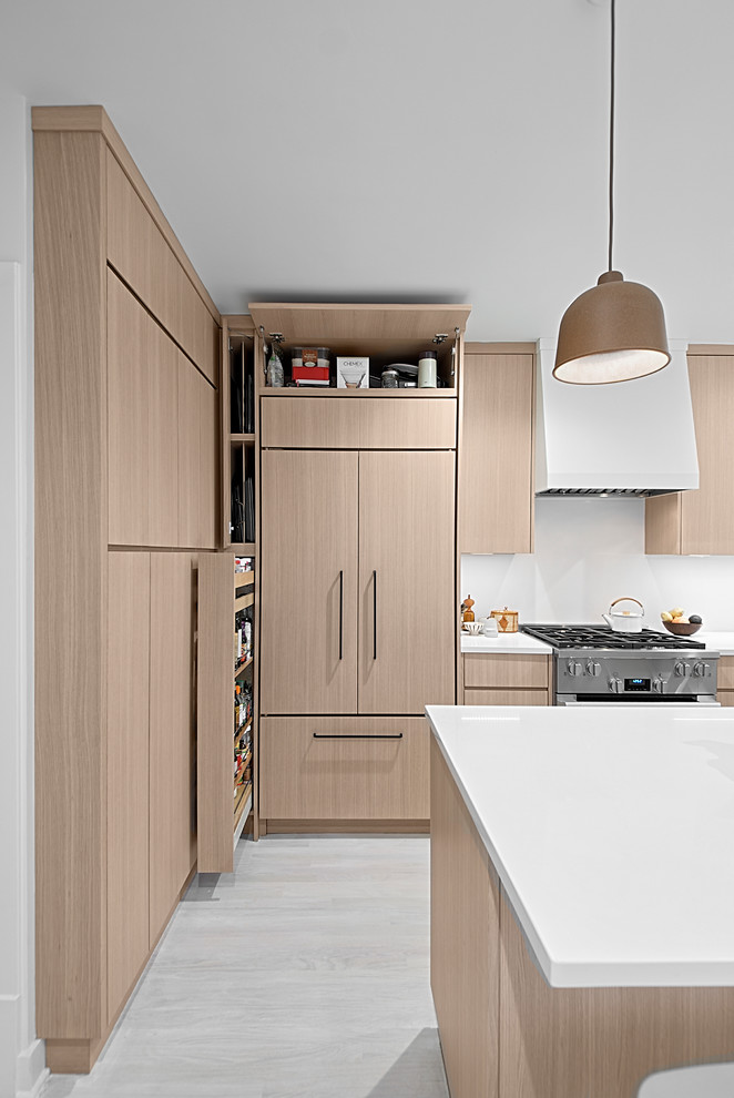 This is an example of a small contemporary u-shaped separate kitchen in Chicago with flat-panel cabinets, light wood cabinets, quartz benchtops, white splashback, stone slab splashback, stainless steel appliances, light hardwood floors, with island, grey floor and white benchtop.