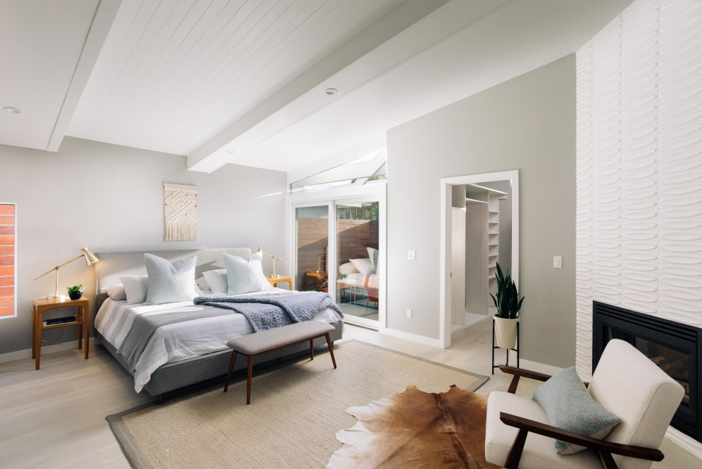 This is an example of a midcentury bedroom in Los Angeles with grey walls, light hardwood floors, a corner fireplace, a tile fireplace surround, beige floor and vaulted.