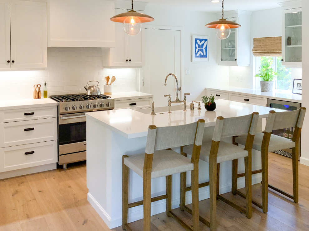 Cottage u-shaped beige floor eat-in kitchen photo with a farmhouse sink, shaker cabinets, white cabinets, quartzite countertops, white backsplash, ceramic backsplash, stainless steel appliances, an island and white countertops