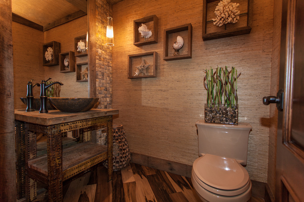 Small tropical powder room in Orange County with a vessel sink, open cabinets, wood benchtops, multi-coloured tile, beige tile, beige walls, medium hardwood floors, distressed cabinets, a two-piece toilet, stone tile, brown floor and brown benchtops.