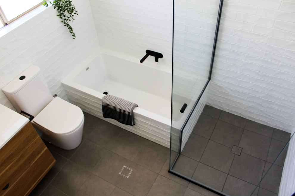 Small modern ensuite bathroom in Perth with flat-panel cabinets, dark wood cabinets, a built-in bath, a corner shower, a one-piece toilet, white tiles, ceramic tiles, white walls, porcelain flooring, a vessel sink, engineered stone worktops, grey floors, a hinged door and white worktops.