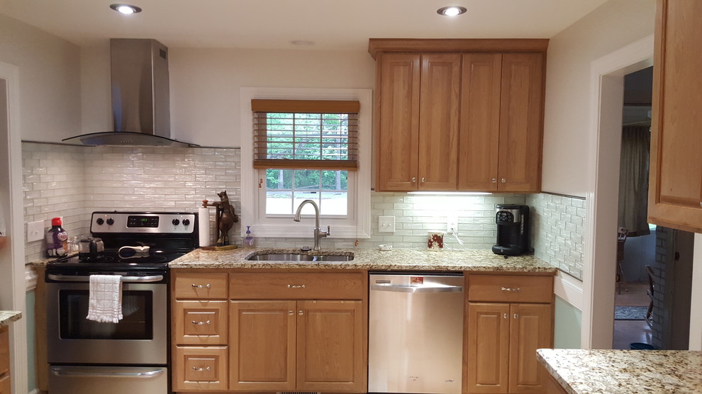 Example of a small transitional u-shaped medium tone wood floor eat-in kitchen design with an undermount sink, raised-panel cabinets, medium tone wood cabinets, granite countertops, white backsplash, glass tile backsplash, stainless steel appliances and no island