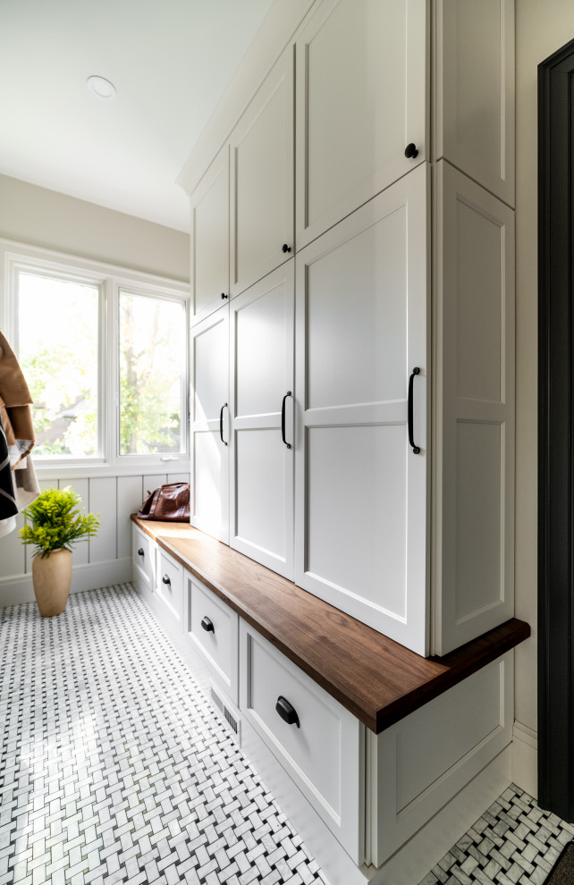 Inspiration for a mid-sized transitional u-shaped brown floor, marble floor and shiplap wall mudroom remodel in Detroit with a farmhouse sink, shaker cabinets, light wood cabinets, soapstone countertops, white backsplash, terra-cotta backsplash, black appliances, an island, black countertops, white walls and a black front door