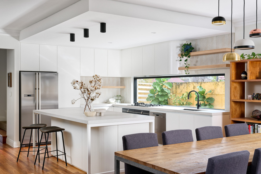 Design ideas for a large scandinavian l-shaped open plan kitchen in Perth with a submerged sink, flat-panel cabinets, white cabinets, engineered stone countertops, beige splashback, porcelain splashback, black appliances, medium hardwood flooring, an island, brown floors and white worktops.