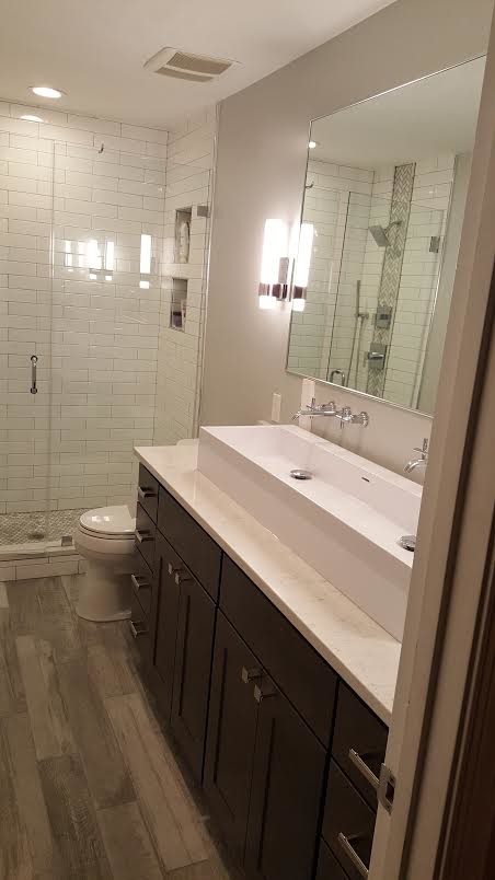 Inspiration for a mid-sized contemporary 3/4 bathroom in DC Metro with shaker cabinets, dark wood cabinets, an alcove shower, a two-piece toilet, white tile, porcelain tile, grey walls, light hardwood floors, a trough sink, limestone benchtops, beige floor and a hinged shower door.