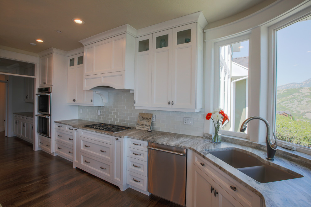 Inspiration for a large transitional open plan kitchen in Salt Lake City with an undermount sink, shaker cabinets, white cabinets, white splashback, subway tile splashback, panelled appliances, medium hardwood floors and with island.