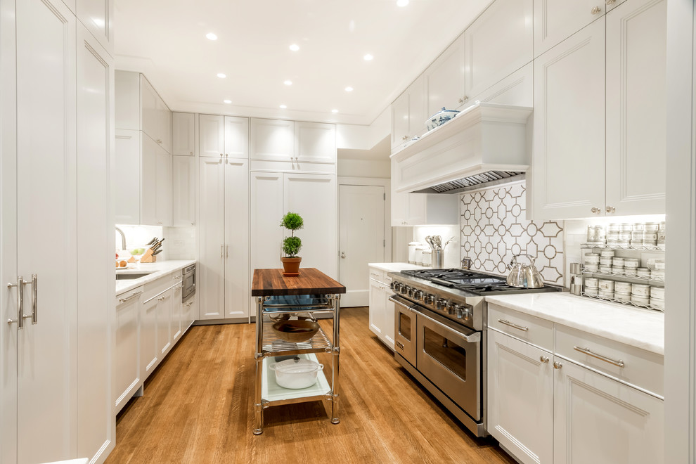 Traditional galley kitchen in New York with an undermount sink, recessed-panel cabinets, white cabinets, multi-coloured splashback, stainless steel appliances, medium hardwood floors and with island.