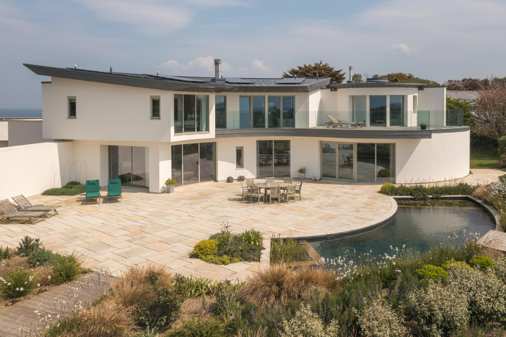 Large beach style two-storey stucco white house exterior in Cornwall with a flat roof, a metal roof and a grey roof.
