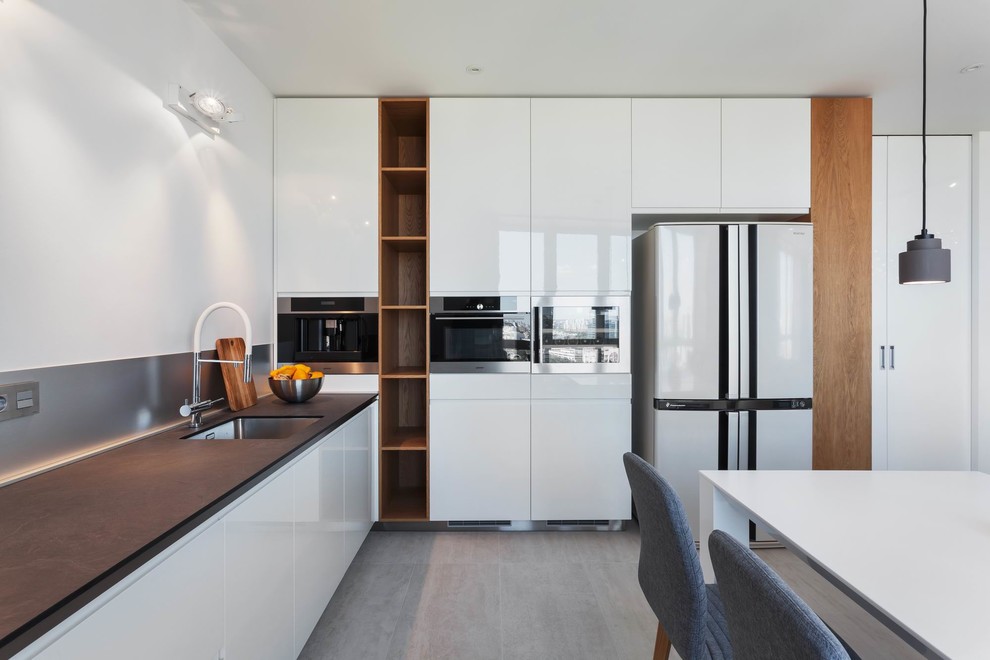 This is an example of a large l-shaped open plan kitchen in Yekaterinburg with flat-panel cabinets, white cabinets, metallic splashback, stainless steel appliances, ceramic floors, no island and grey floor.