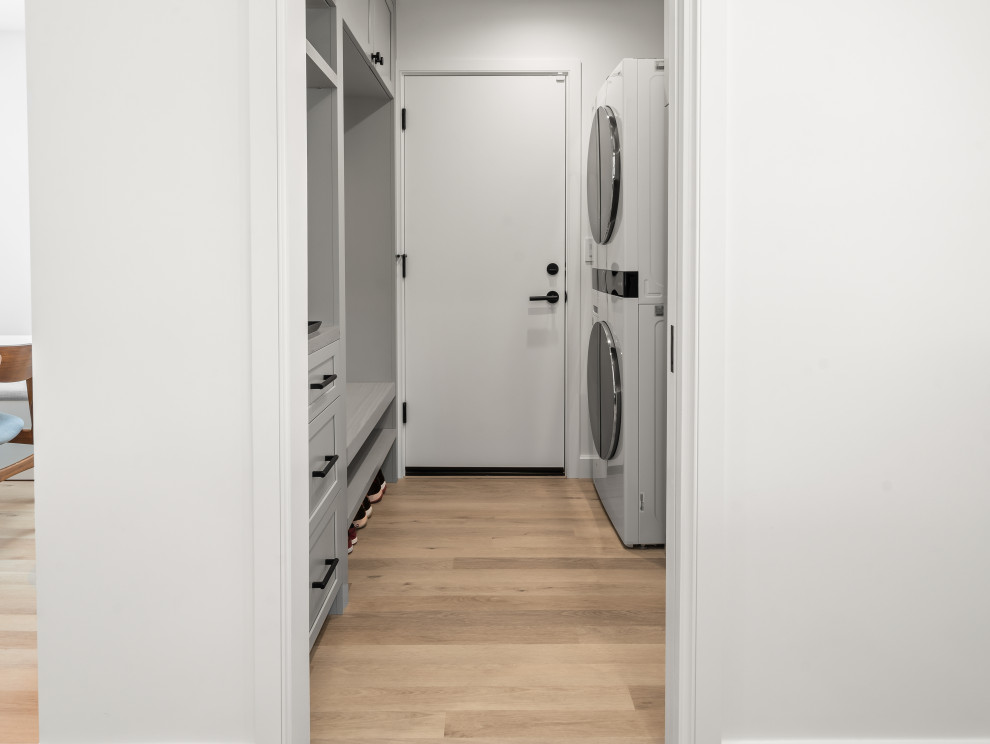 Mid-sized scandinavian l-shaped laundry cupboard in San Francisco with a drop-in sink, open cabinets, grey cabinets, marble benchtops, white splashback, marble splashback, white walls, vinyl floors, a stacked washer and dryer, beige floor, white benchtop and vaulted.