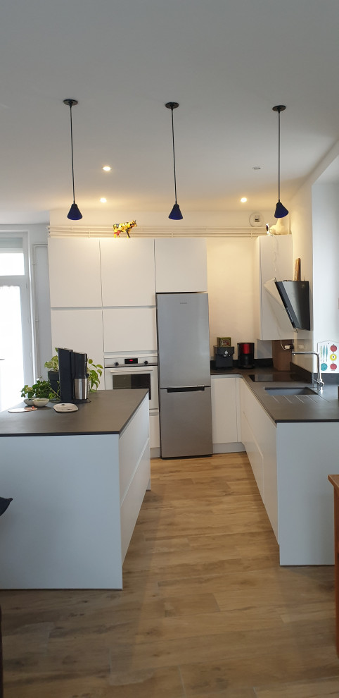 Photo of a mid-sized modern l-shaped open plan kitchen in Toulouse with an integrated sink, beaded inset cabinets, stainless steel cabinets, quartzite benchtops, white splashback, glass tile splashback, coloured appliances, medium hardwood floors, with island, brown floor and black benchtop.