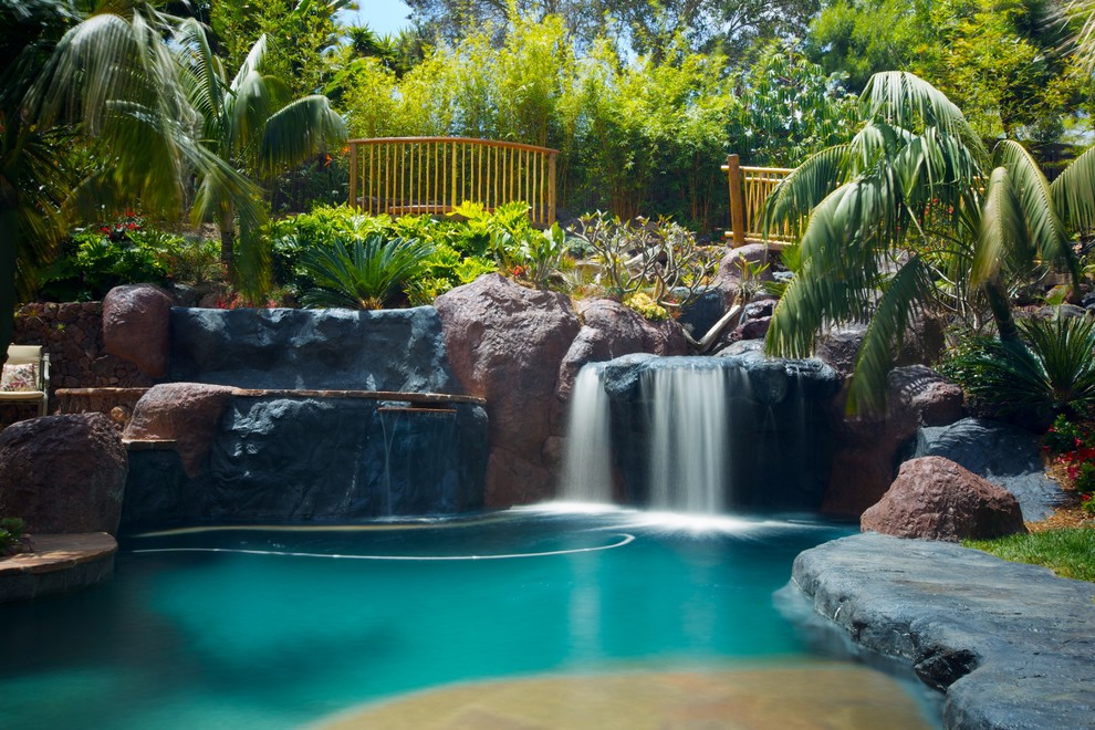 Inspiration for a large tropical backyard custom-shaped pool in San Diego with a water feature and natural stone pavers.
