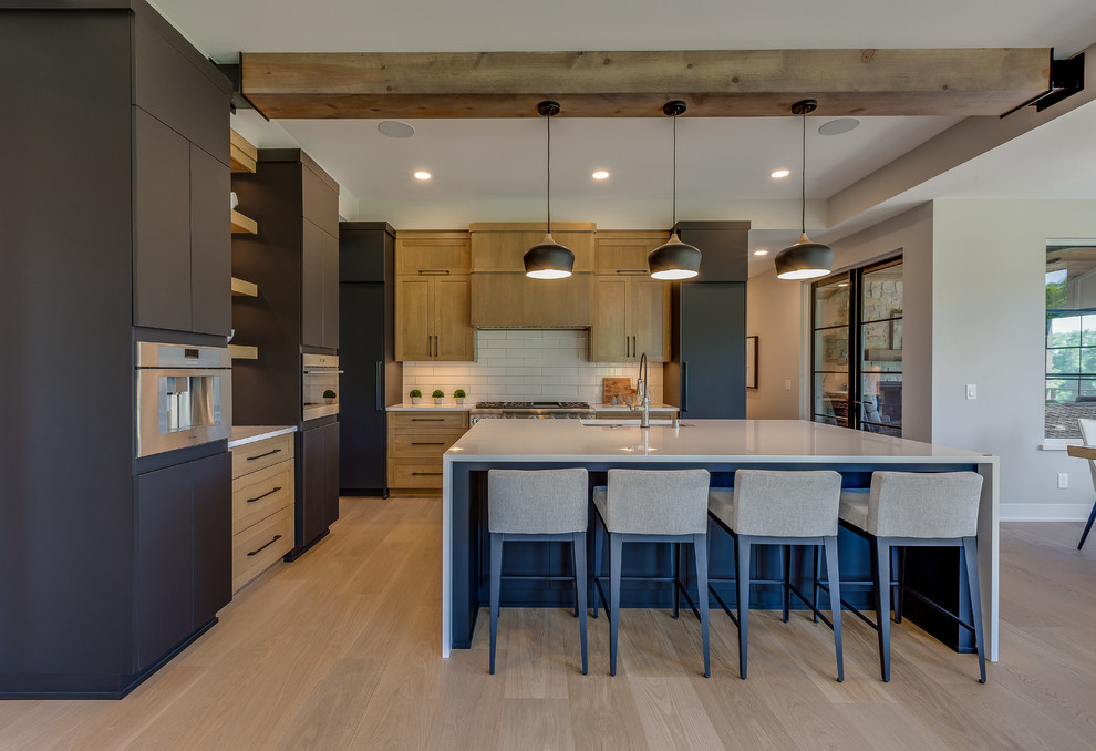 This is an example of a large transitional kitchen in Minneapolis with an undermount sink, quartz benchtops, white splashback, porcelain splashback, stainless steel appliances, light hardwood floors, with island, beige floor, white benchtop, shaker cabinets and medium wood cabinets.