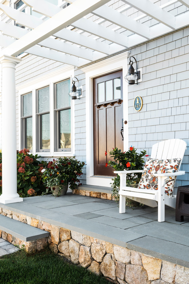 Small beach style front yard verandah in Boston with natural stone pavers and a pergola.