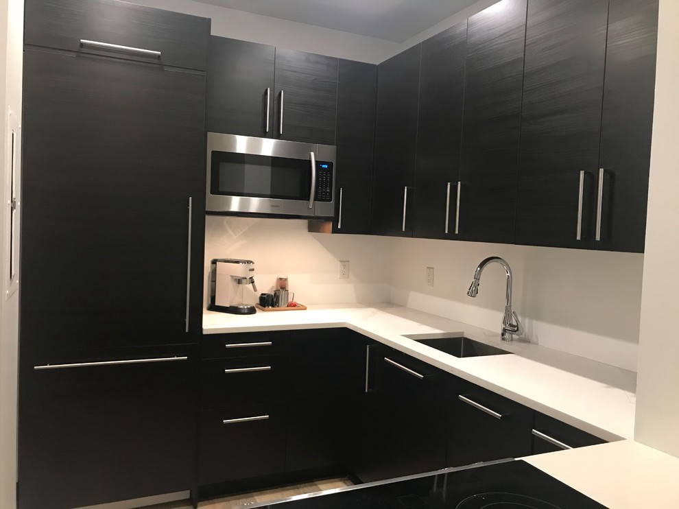 This is an example of a small contemporary u-shaped separate kitchen in New York with an undermount sink, flat-panel cabinets, black cabinets, quartz benchtops, white splashback, panelled appliances, laminate floors, no island, beige floor and white benchtop.