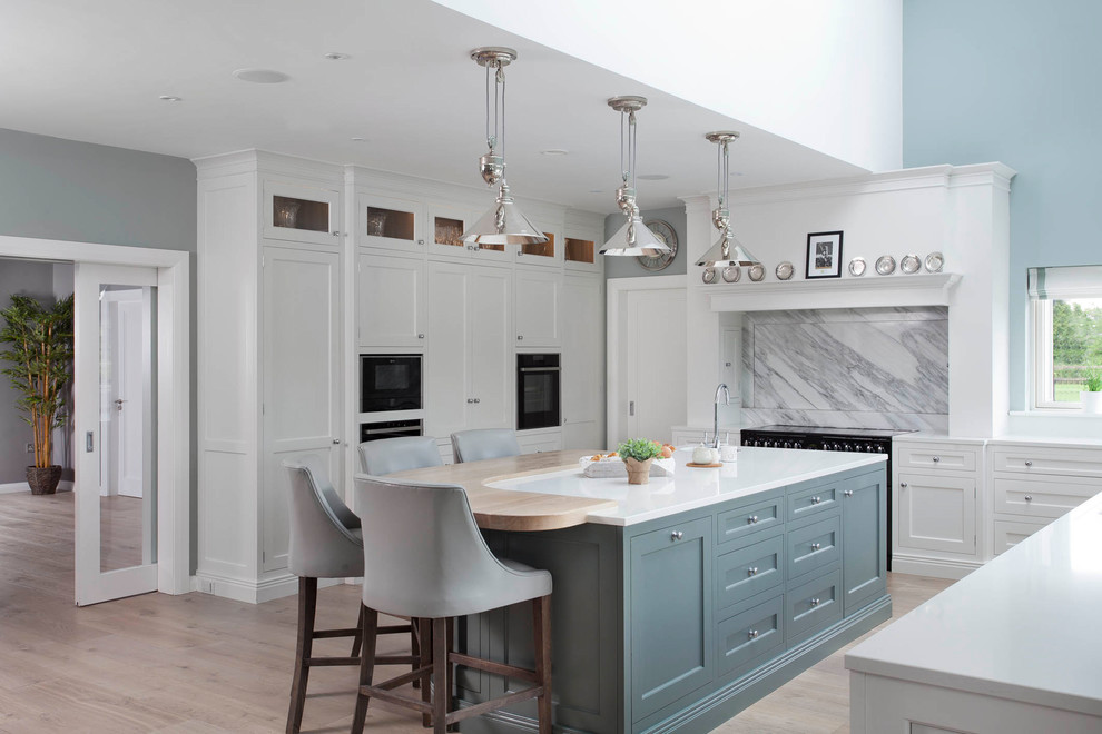 This is an example of a large transitional u-shaped open plan kitchen in Other with an integrated sink, shaker cabinets, white cabinets, quartzite benchtops, grey splashback, marble splashback, black appliances, medium hardwood floors, with island, brown floor and white benchtop.