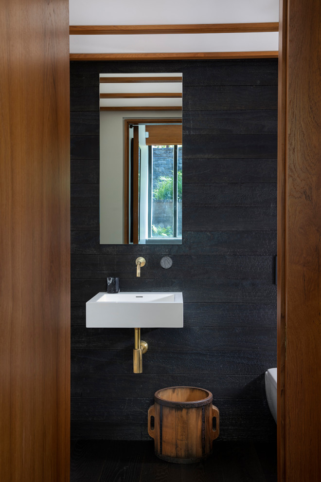 Idée de décoration pour un WC et toilettes design en bois avec un mur noir et un lavabo suspendu.