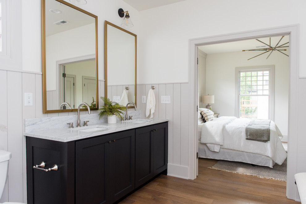Inspiration for a mid-sized transitional master marble tile medium tone wood floor, brown floor, double-sink and wainscoting bathroom remodel in Indianapolis with shaker cabinets, black cabinets, an undermount sink, marble countertops, white walls, gray countertops and a built-in vanity