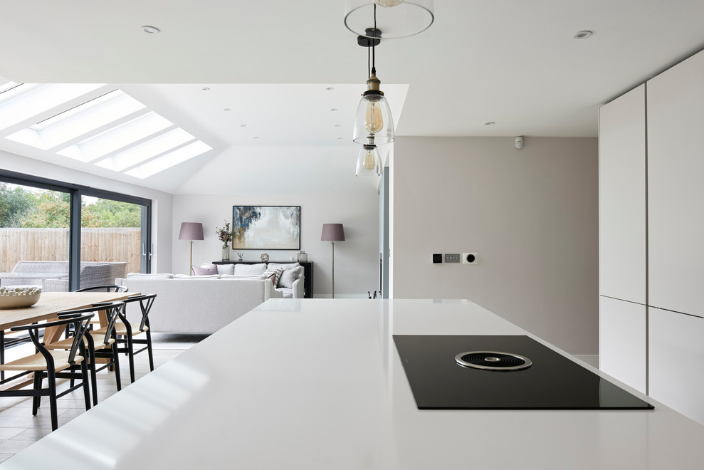 Large contemporary l-shaped open plan kitchen in Hertfordshire with ceramic floors, with island, white floor and white benchtop.