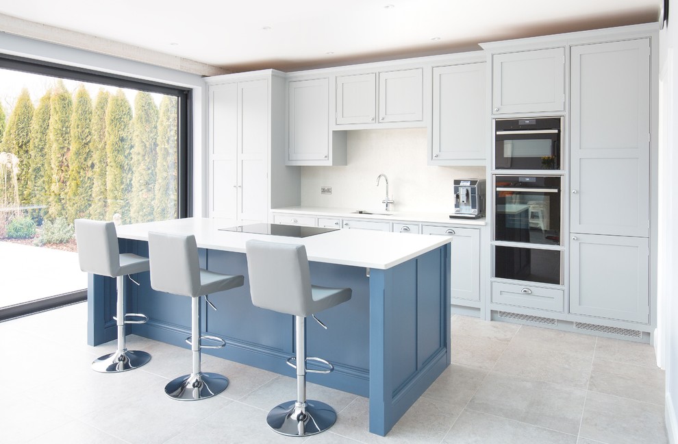 Design ideas for a large transitional single-wall kitchen in Surrey with a single-bowl sink, grey cabinets, quartzite benchtops, white splashback, ceramic floors, with island, white benchtop, beaded inset cabinets, black appliances and grey floor.
