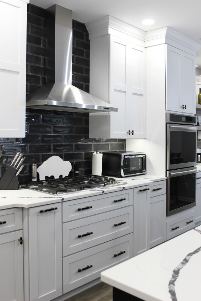 Example of a large transitional single-wall vinyl floor and beige floor eat-in kitchen design with a farmhouse sink, shaker cabinets, white cabinets, quartz countertops, black backsplash, subway tile backsplash, stainless steel appliances, an island and white countertops