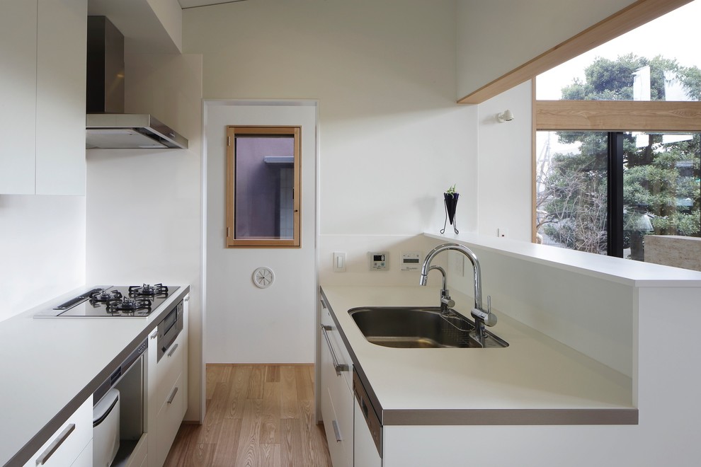 Small modern galley open plan kitchen in Tokyo with an undermount sink, flat-panel cabinets, white cabinets, white splashback, glass sheet splashback, black appliances, plywood floors, with island, beige floor and white benchtop.