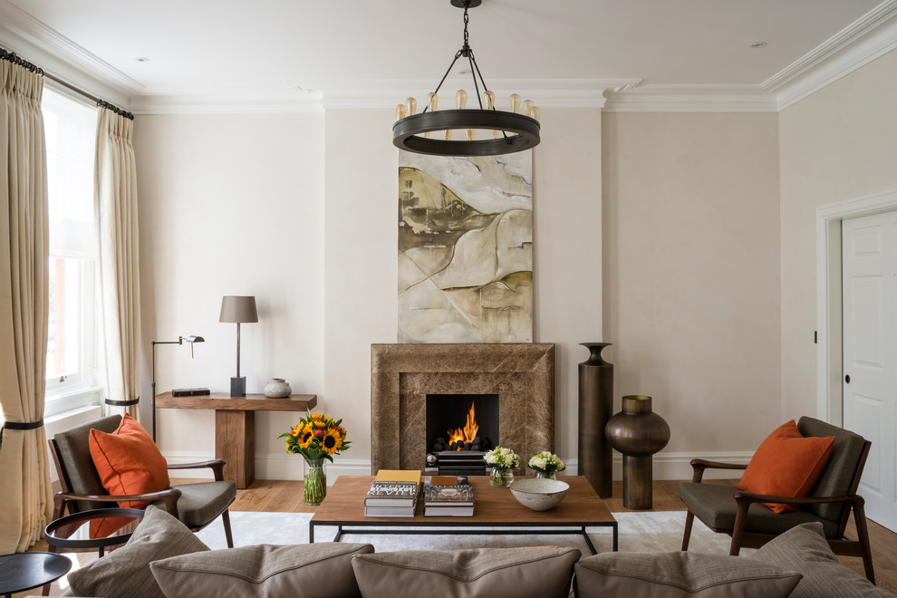 This is an example of a transitional living room in London with beige walls, dark hardwood floors and a standard fireplace.