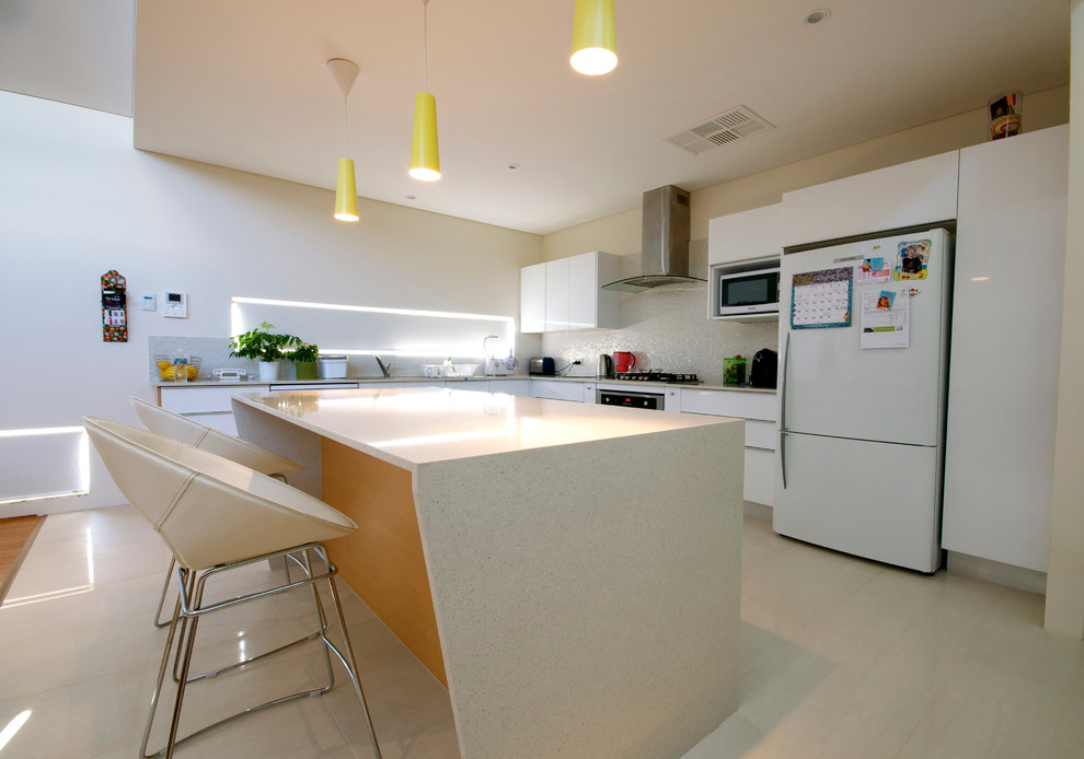 This is an example of a mid-sized midcentury l-shaped eat-in kitchen in Perth with an undermount sink, flat-panel cabinets, white cabinets, solid surface benchtops, white splashback, ceramic splashback, stainless steel appliances, ceramic floors and with island.