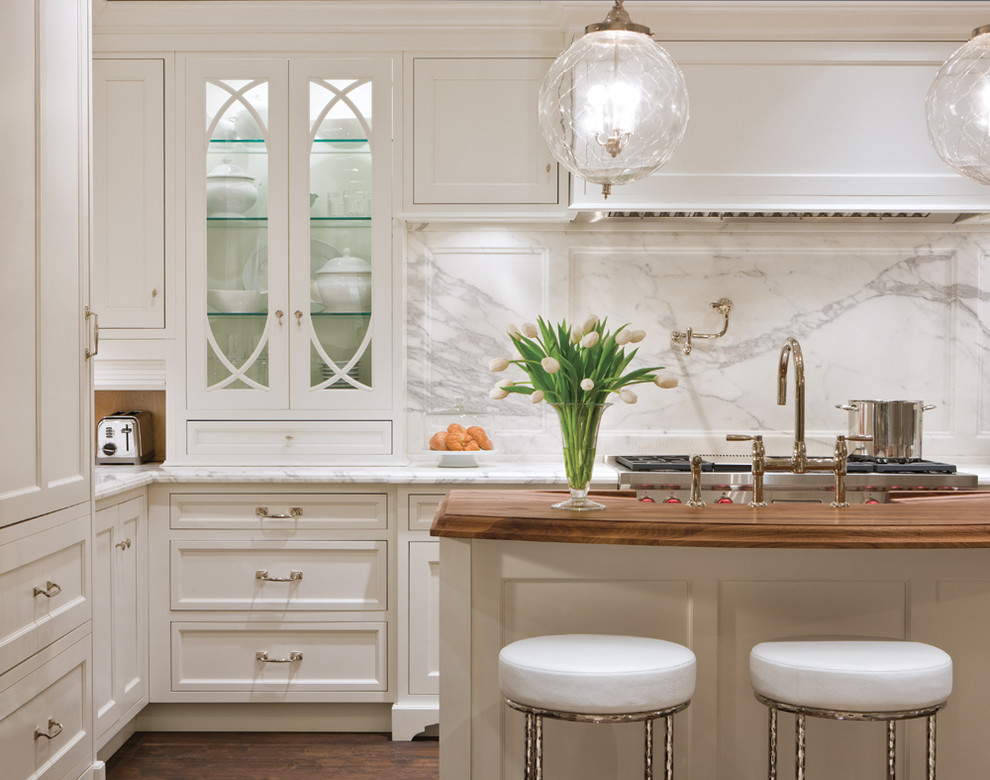 This is an example of a traditional kitchen in Chicago with glass-front cabinets, marble benchtops, white splashback, with island, white cabinets and marble splashback.