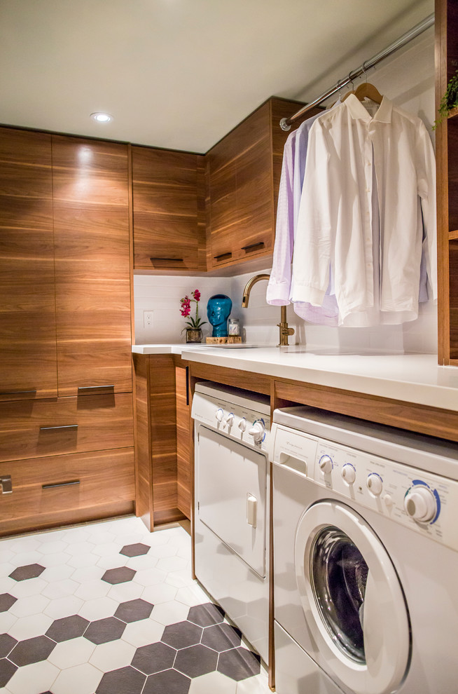 Small modern l-shaped dedicated laundry room in Toronto with a single-bowl sink, flat-panel cabinets, medium wood cabinets, solid surface benchtops, white walls, porcelain floors and a side-by-side washer and dryer.