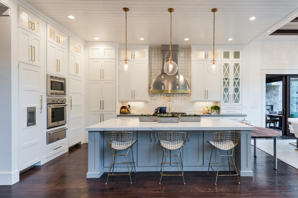 Inspiration for a mid-sized transitional l-shaped dark wood floor and brown floor eat-in kitchen remodel in Salt Lake City with a farmhouse sink, shaker cabinets, white cabinets, quartz countertops, white backsplash, ceramic backsplash, stainless steel appliances and an island