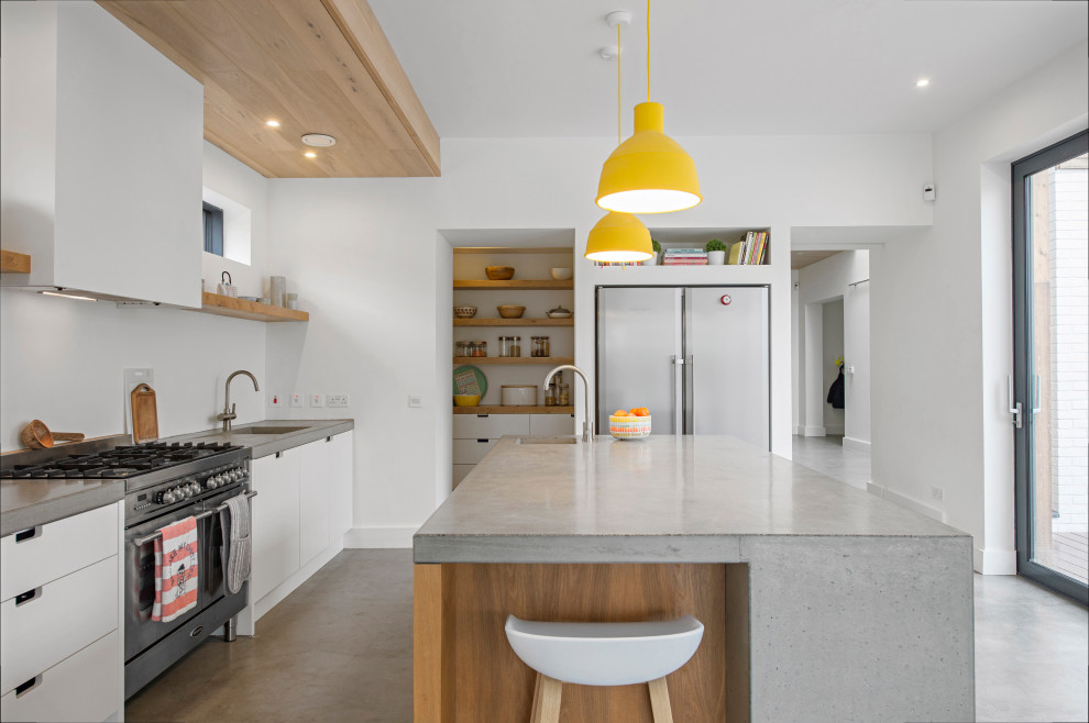 Mid-sized contemporary open plan kitchen in Dublin with a drop-in sink, flat-panel cabinets, white cabinets, concrete benchtops, white splashback, stainless steel appliances, concrete floors, with island, grey floor, grey benchtop and timber.